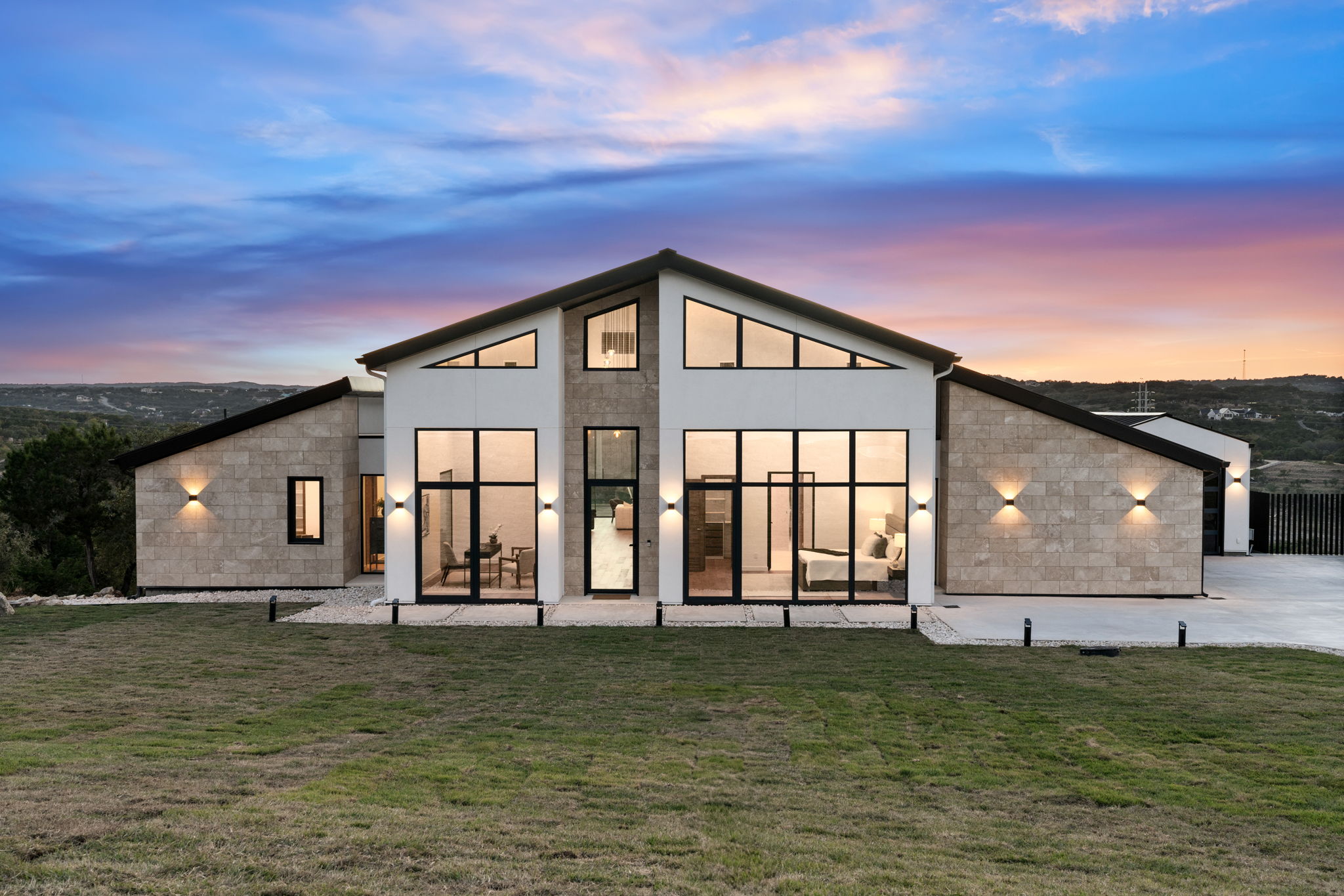 Modern house with large windows and a sloped roof, set against a colorful sunset sky, with a grassy foreground.