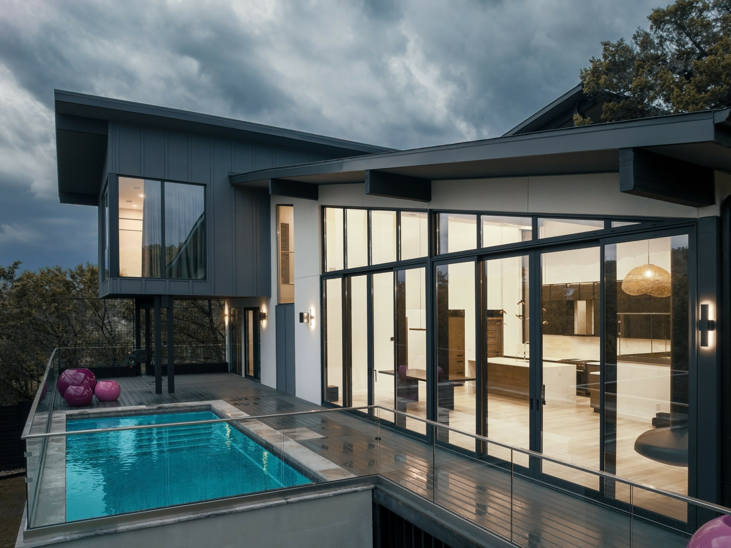 Modern house with large glass windows, outdoor pool, and a deck, under a cloudy sky.