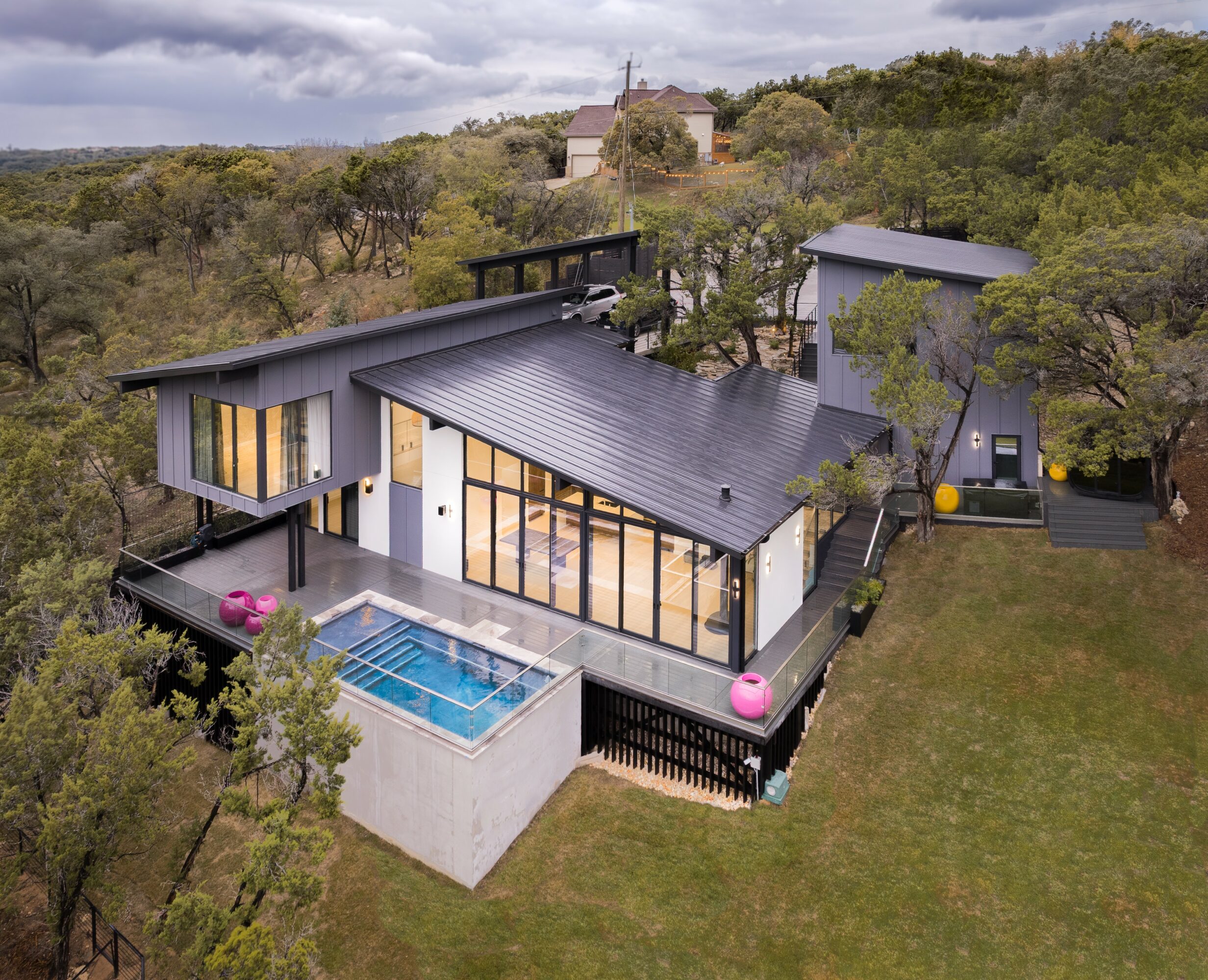 Modern house with large windows, a pool, and a deck surrounded by trees and greenery.
