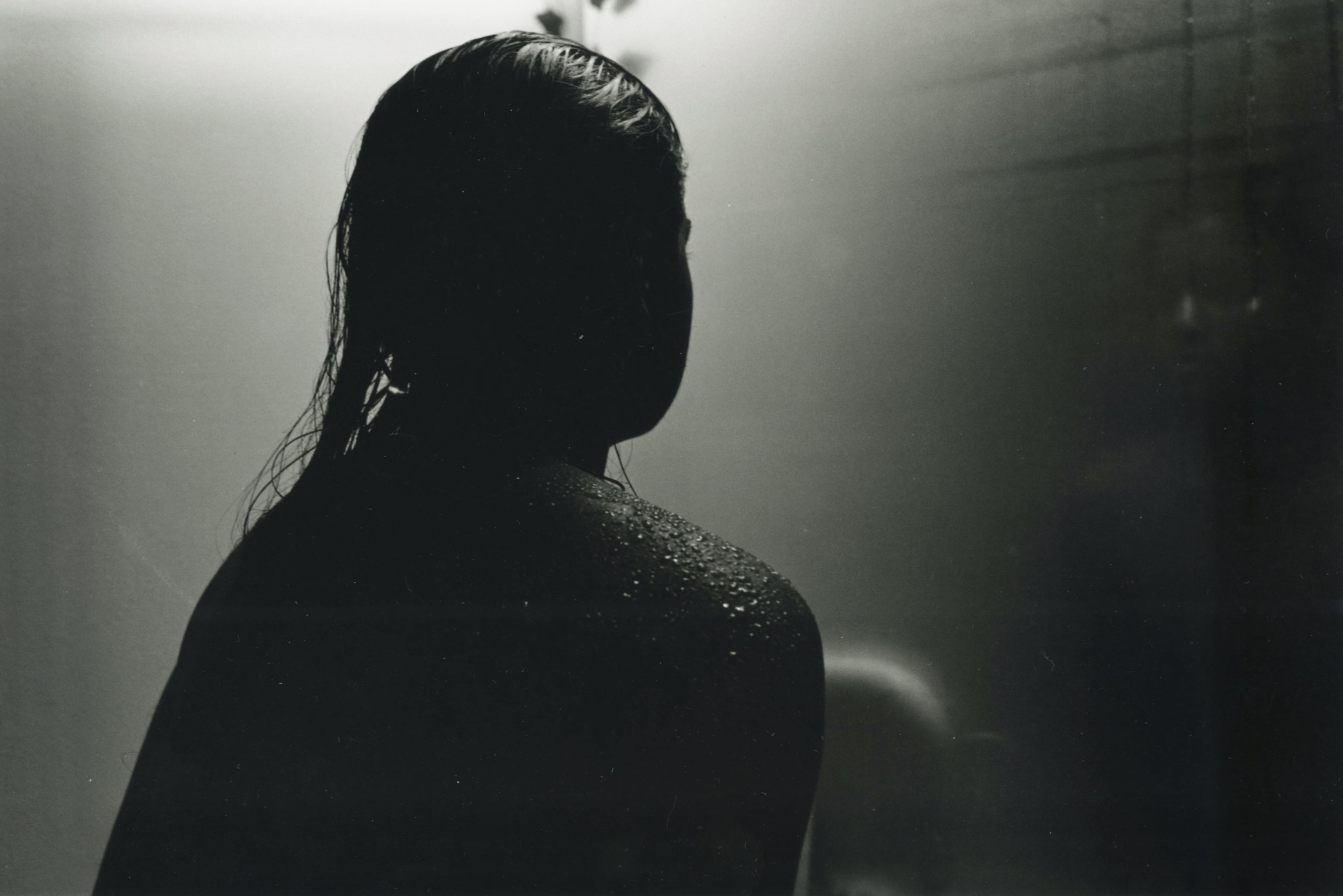 Silhouette of a person with wet hair, facing away, in a dimly lit environment.
