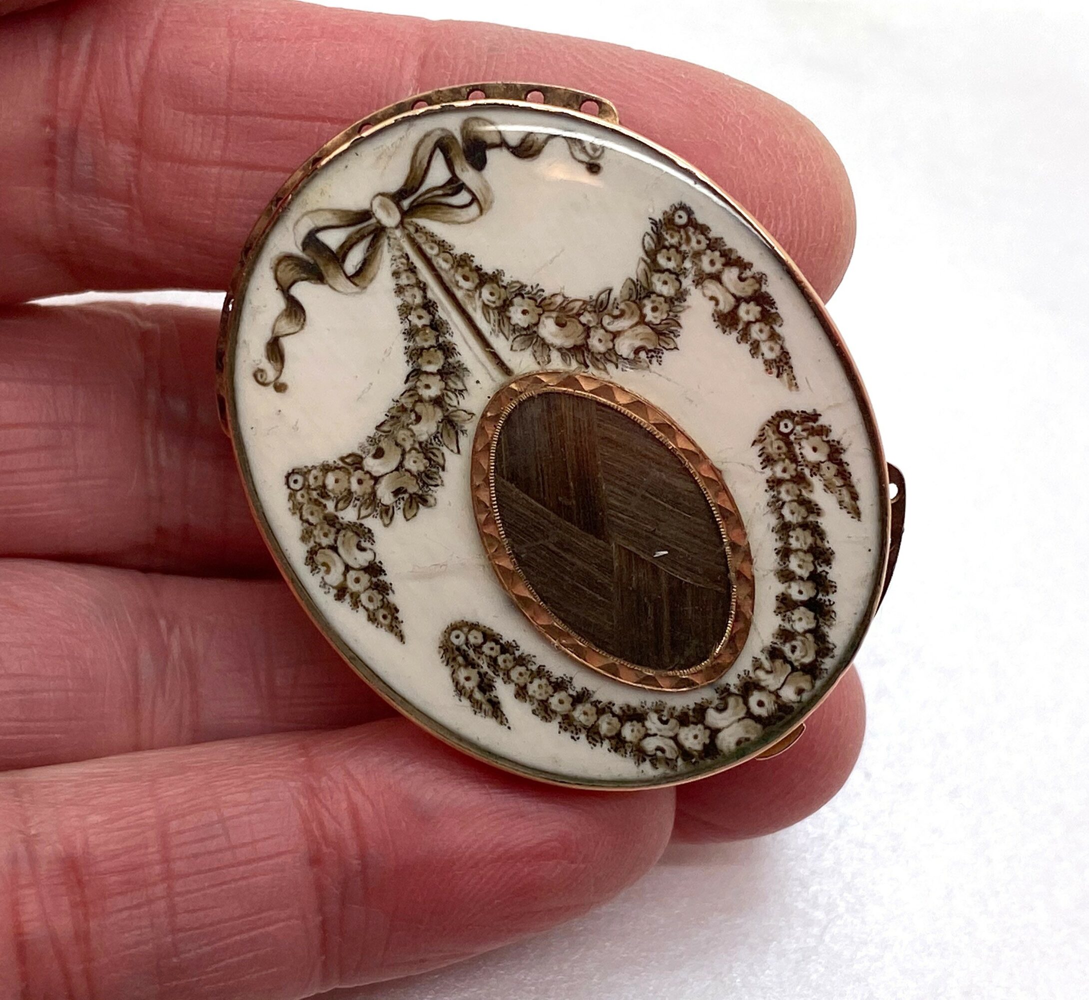 Round decorative object with intricate gold and brown designs, held between fingers, against a white background.