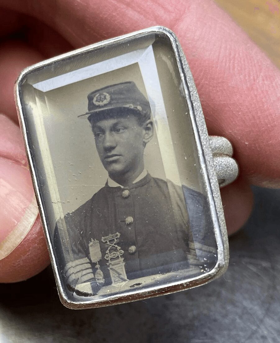 Black and white photo of a young man in a military uniform inside a rectangular case, held by a hand.
