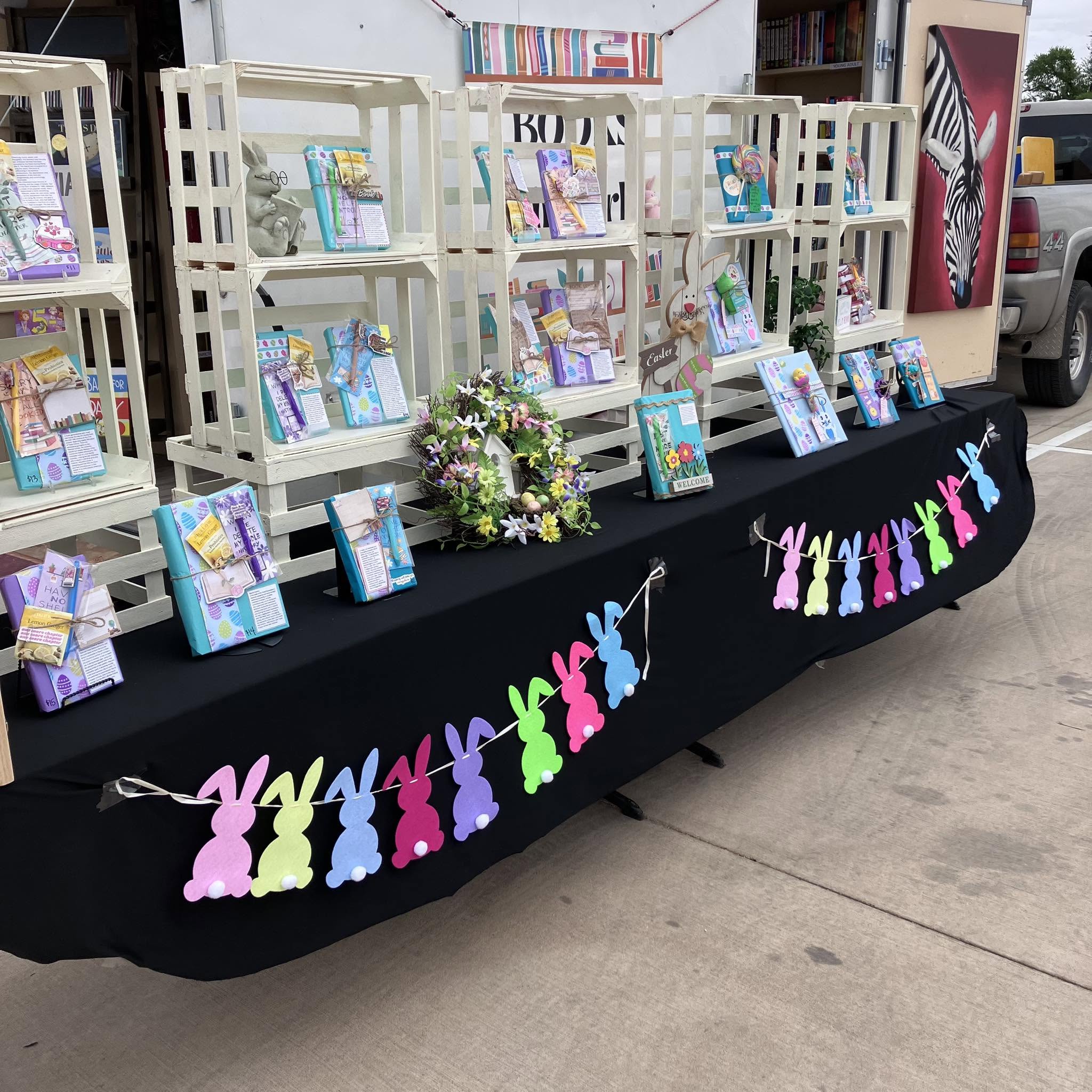 Display of books on white shelves with Easter-themed decorations, including colorful bunny and egg cutouts, on a black tablecloth.
