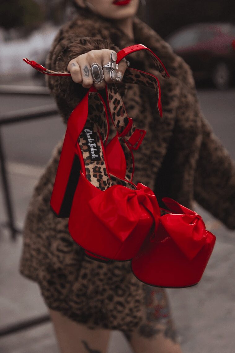 Person holding a red bag with leopard print straps, wearing a leopard print coat, outdoors in an urban setting.