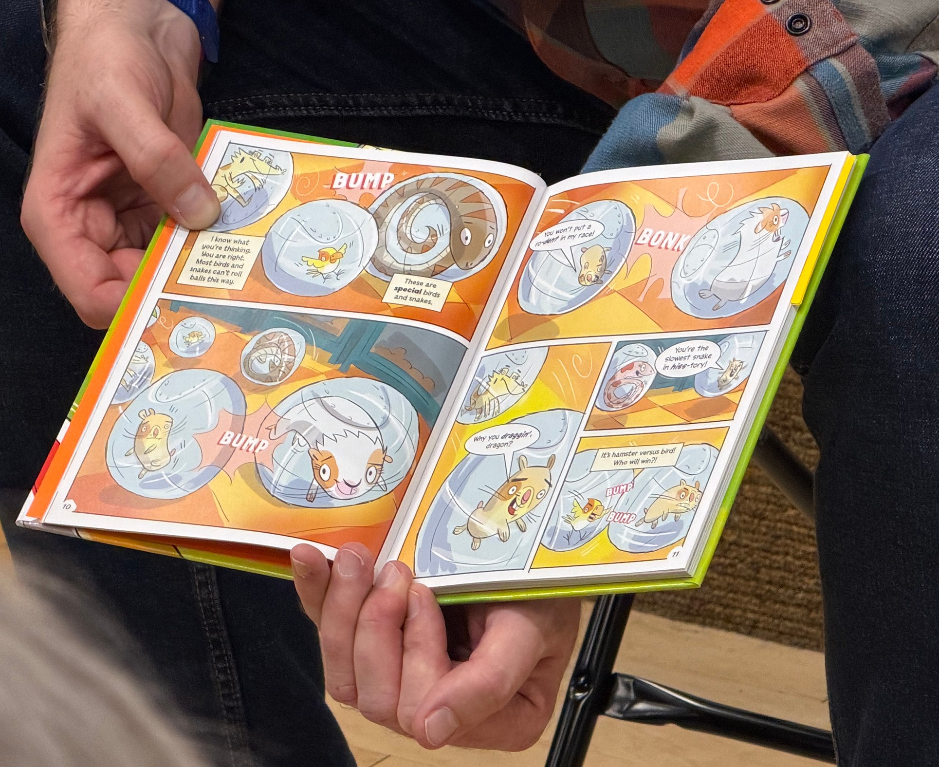 Person holding open comic book with colorful illustrations and speech bubbles, showing a story with animals and objects.