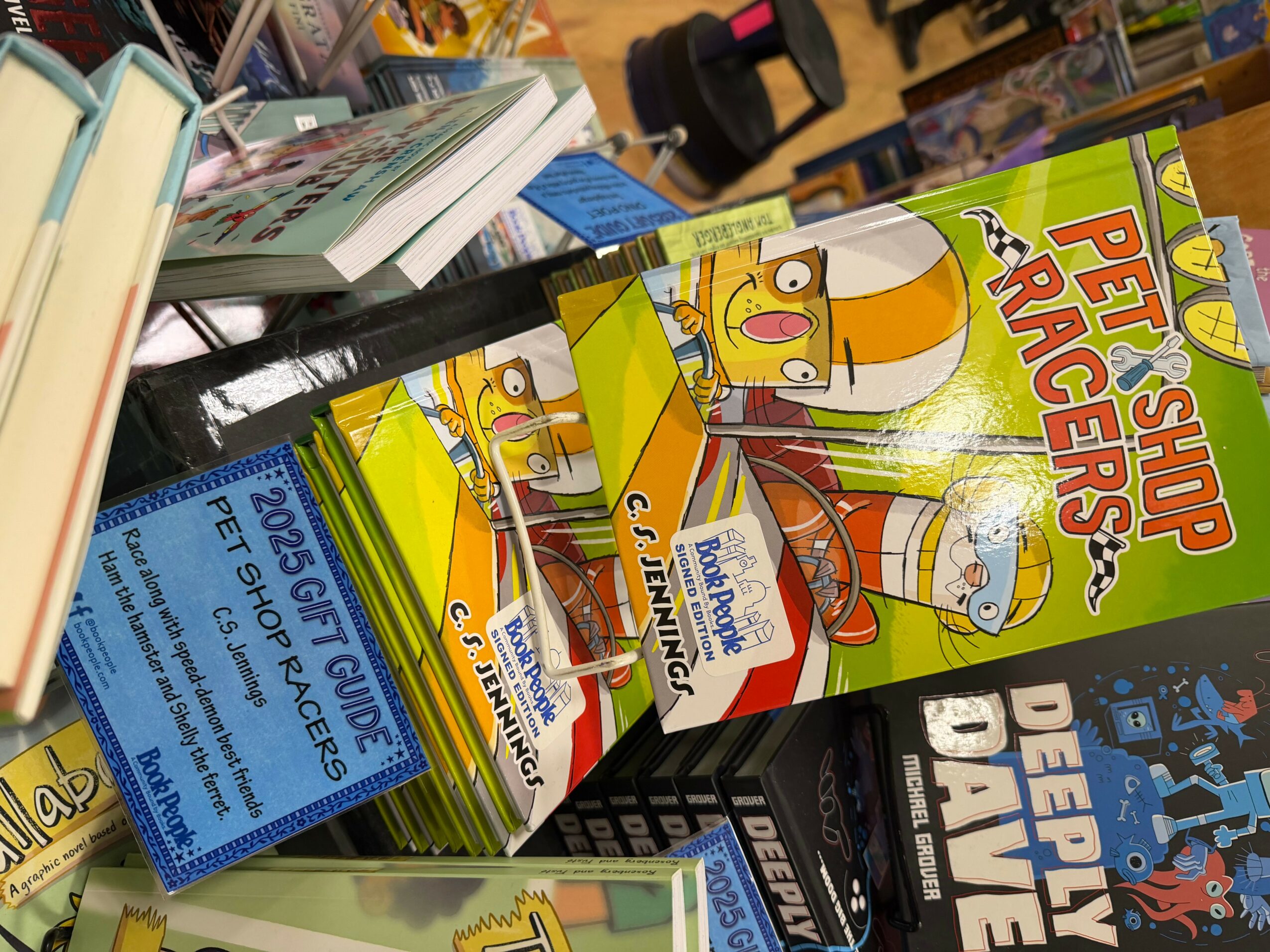 Books and magazines on a shelf, including a pet shop rangers comic and a guidebook, with a blue sign in the foreground.