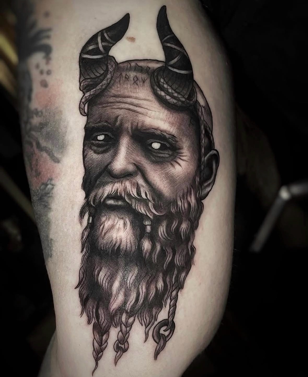 Tattoo of a bearded man with horns and a serious expression on upper arm.