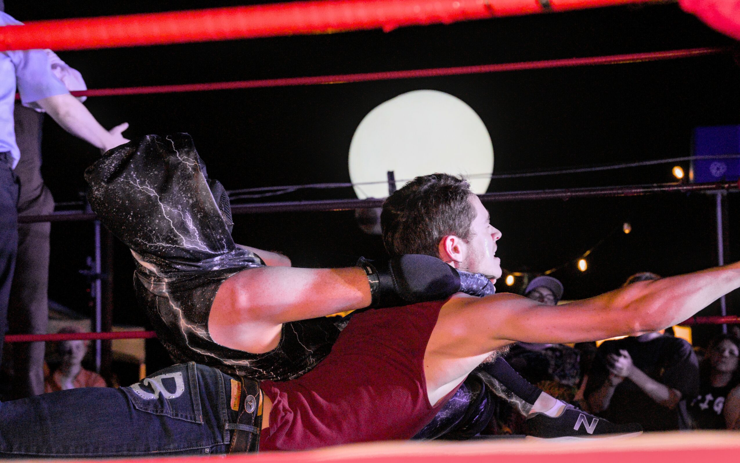 Two women wrestling in a ring at night, with a bright full moon in the background.