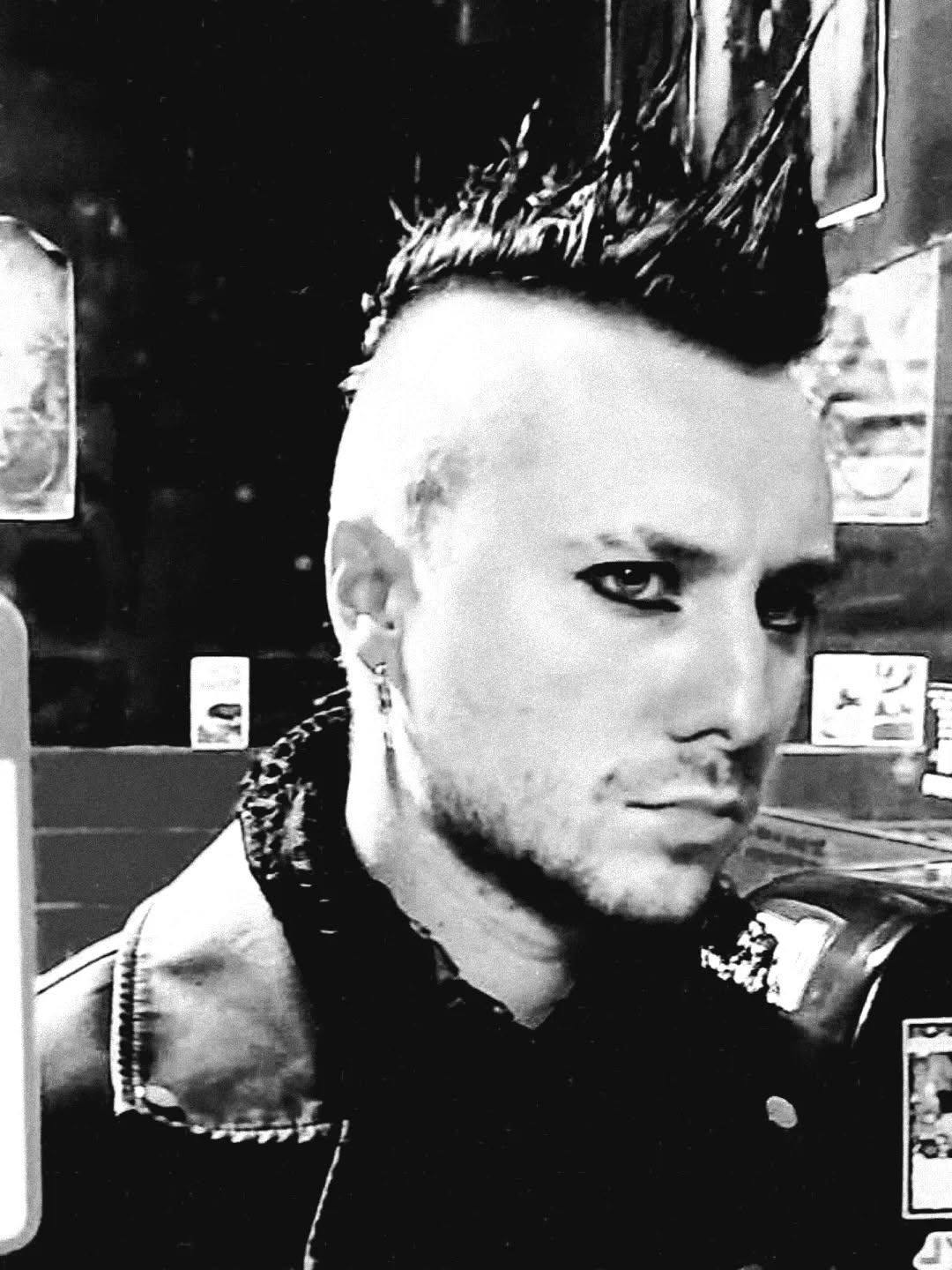 Person with spiked hairstyle and leather jacket looking sideways, in black and white.