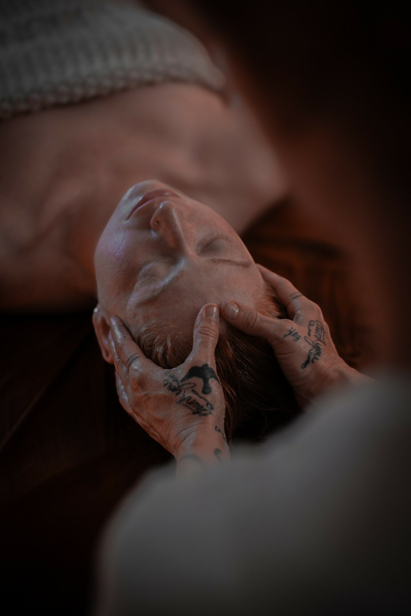 Person gently holding a newborn baby's head, both lying down in a close-up shot.