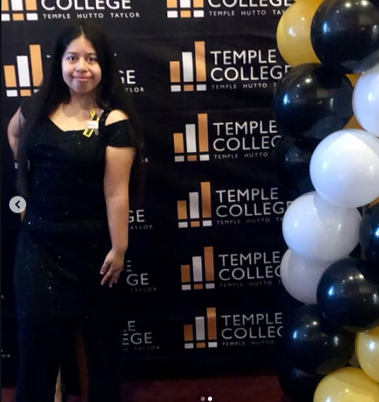 Young woman in black dress standing in front of a black backdrop with balloons on the side.