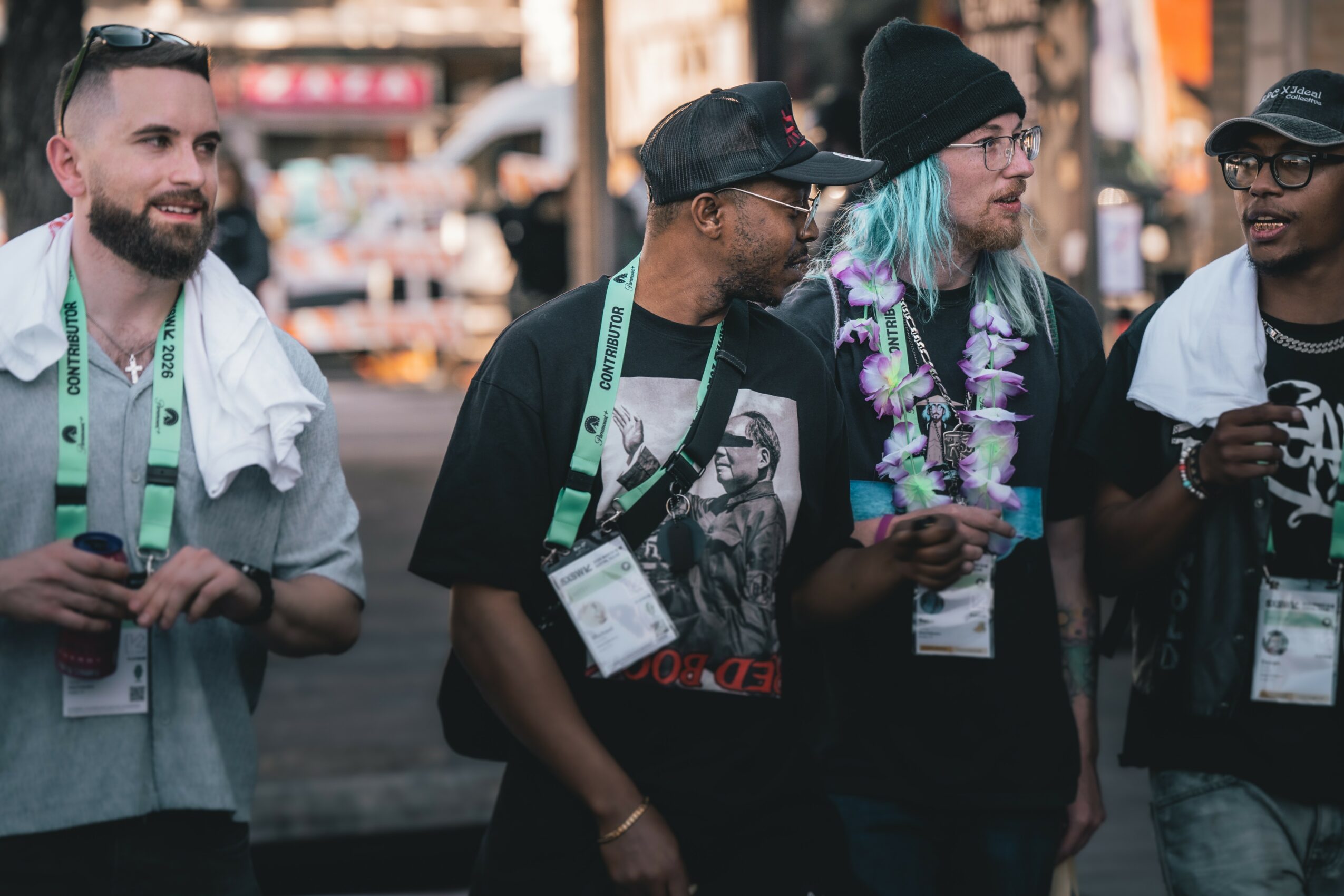 Group of four people standing outdoors, some wearing hats and lanyards, engaged in conversation.