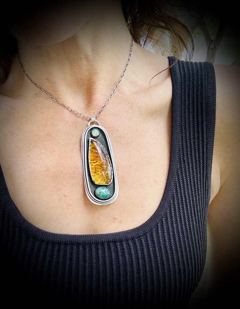 Person wearing a necklace with a pendant containing amber and turquoise, dressed in a black sleeveless top.