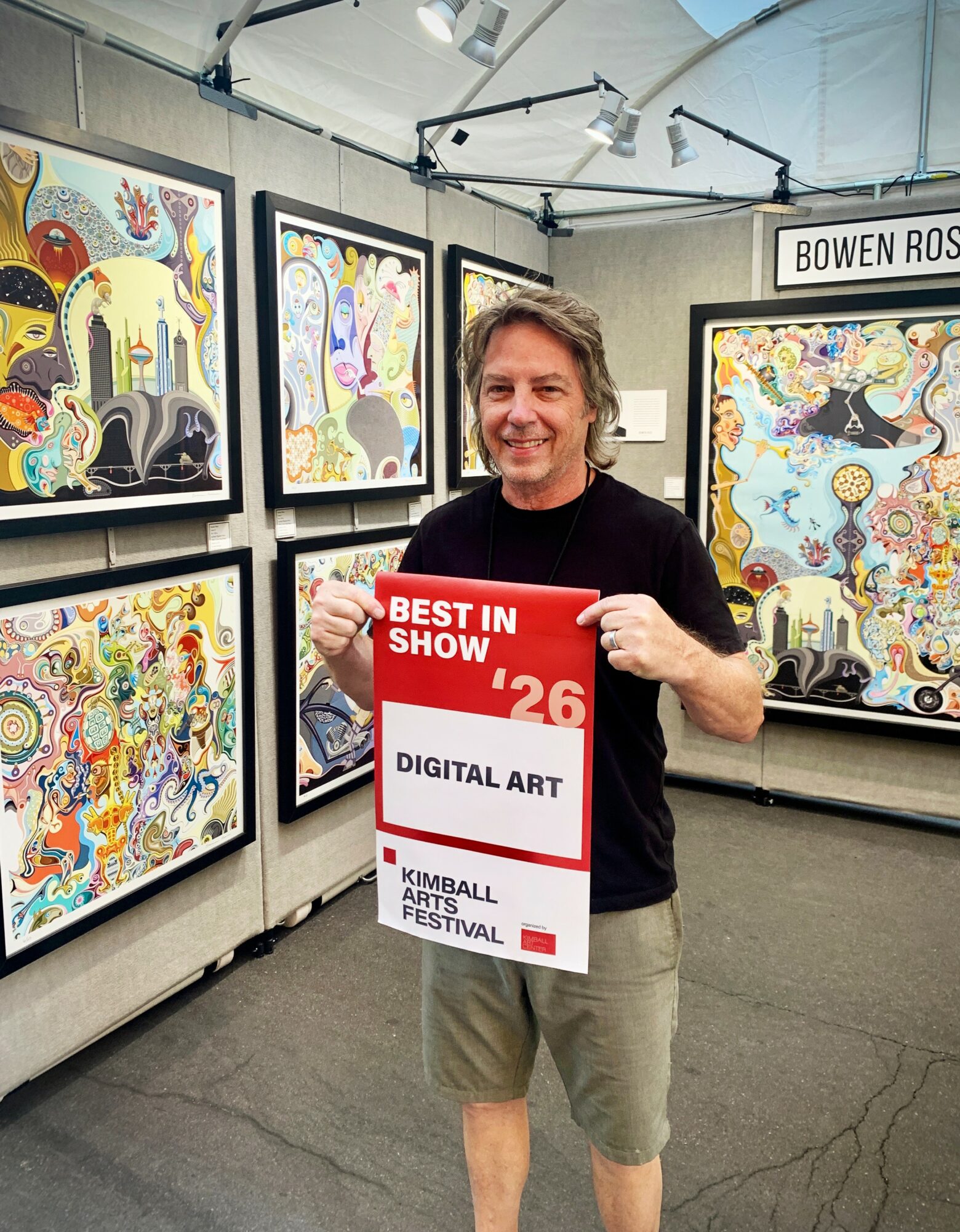 Person holding a red sign at an art exhibition with colorful paintings in the background.
