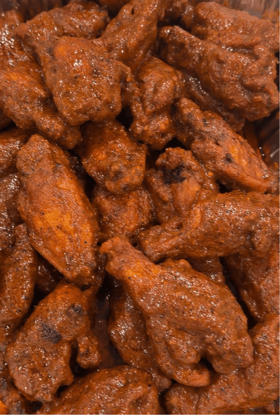 Close-up of fried chicken pieces coated in sauce, showing a crispy texture and reddish-brown color.