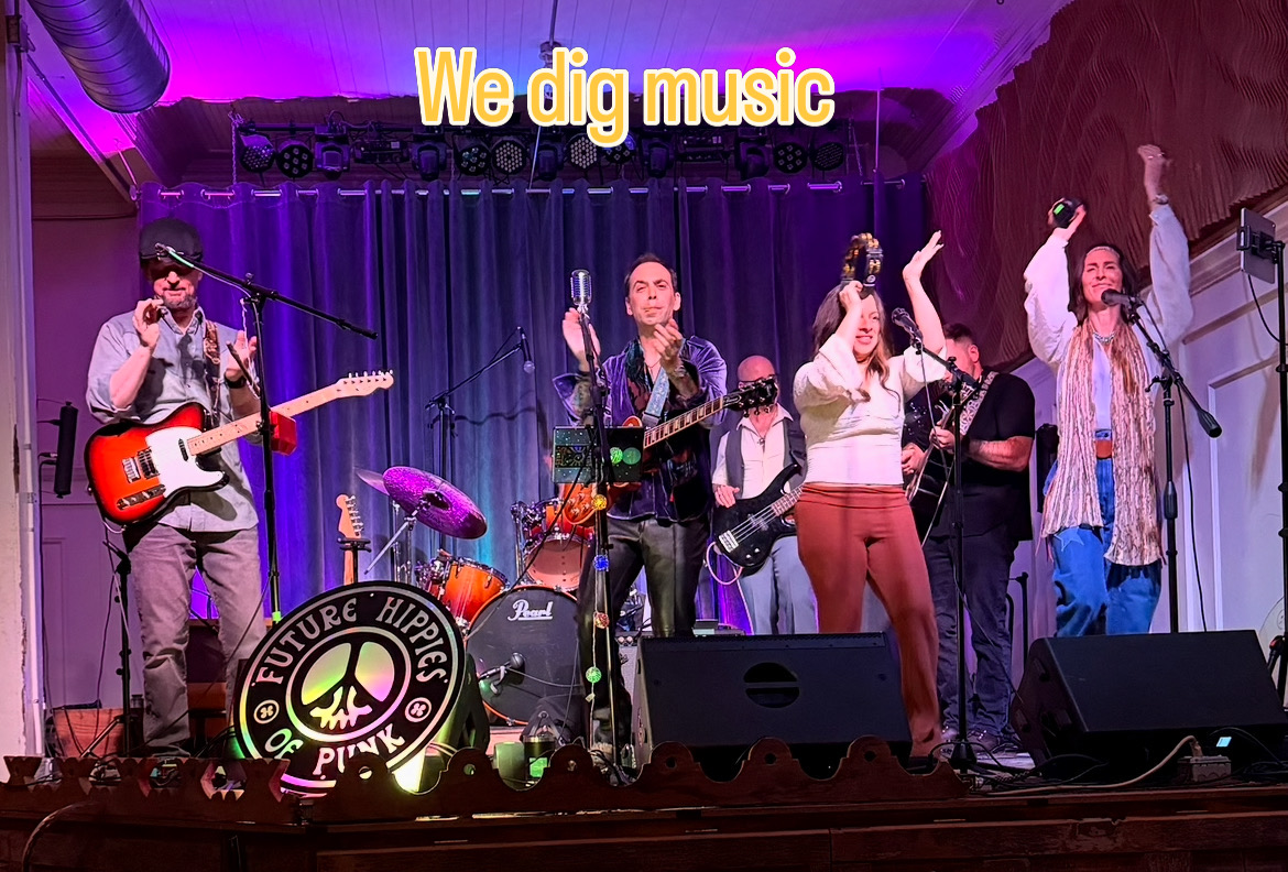 Group of six musicians performing on stage with instruments, colorful lighting, and a sign that says 'We dig music'.