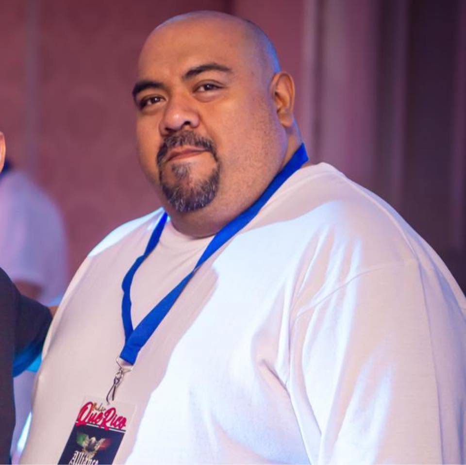 Man with a beard and mustache wearing a white shirt and a blue lanyard, looking at the camera.