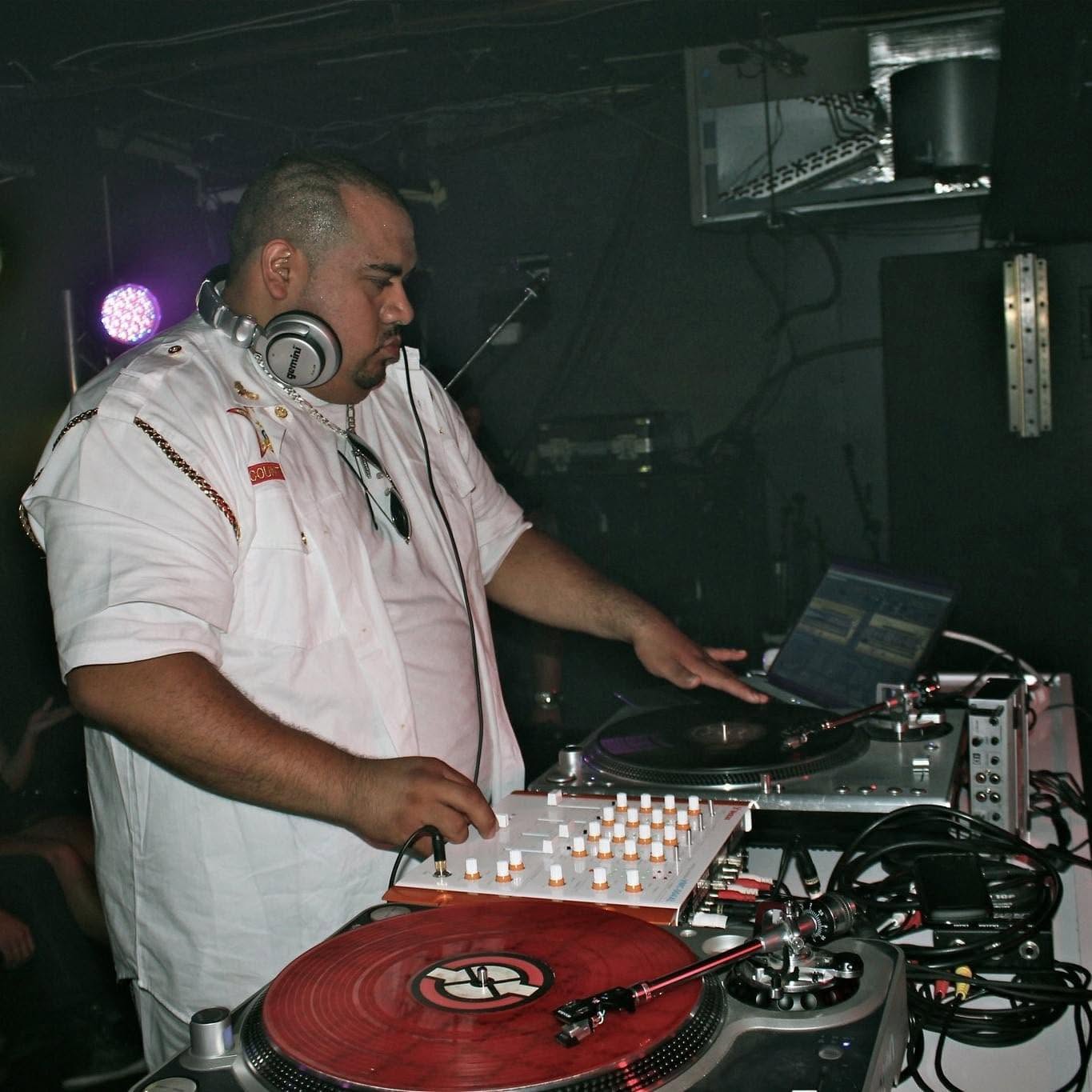 DJ with headphones working at turntables and mixer in a dark club setting.