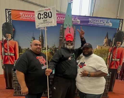 Three men standing indoors in front of a backdrop with toy soldiers and a cityscape, one holding a sign with '0:80' and '10X CONTINUOUS'.