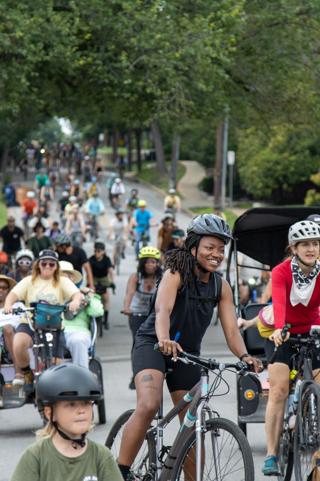 Group of people riding bicycles in a park with trees and a pathway, some wearing helmets and casual clothing.