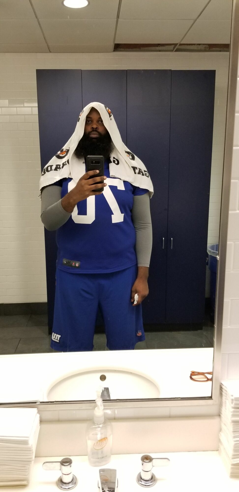 Person taking a mirror selfie in a bathroom, wearing a blue and white uniform, with a sink and mirror visible.