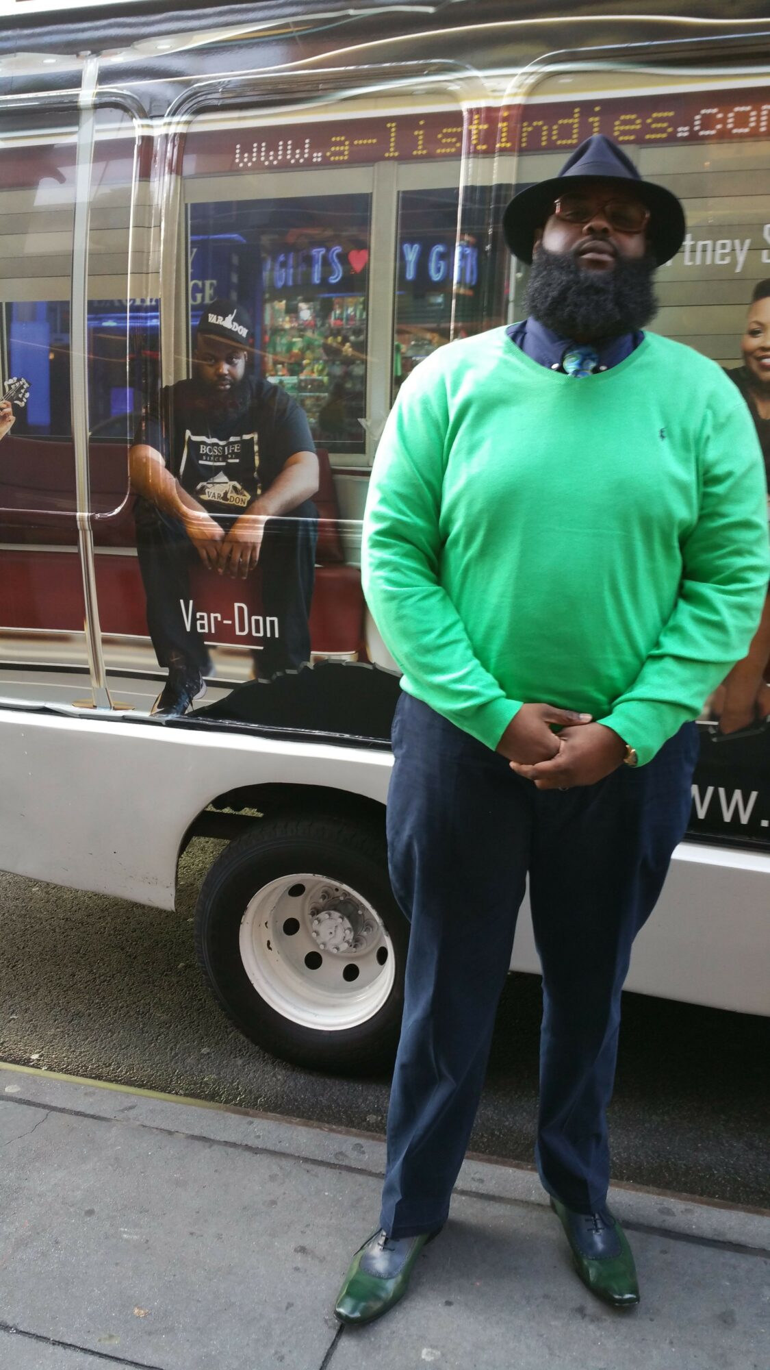 Person in green shirt standing outside near a vehicle, with a storefront in the background.