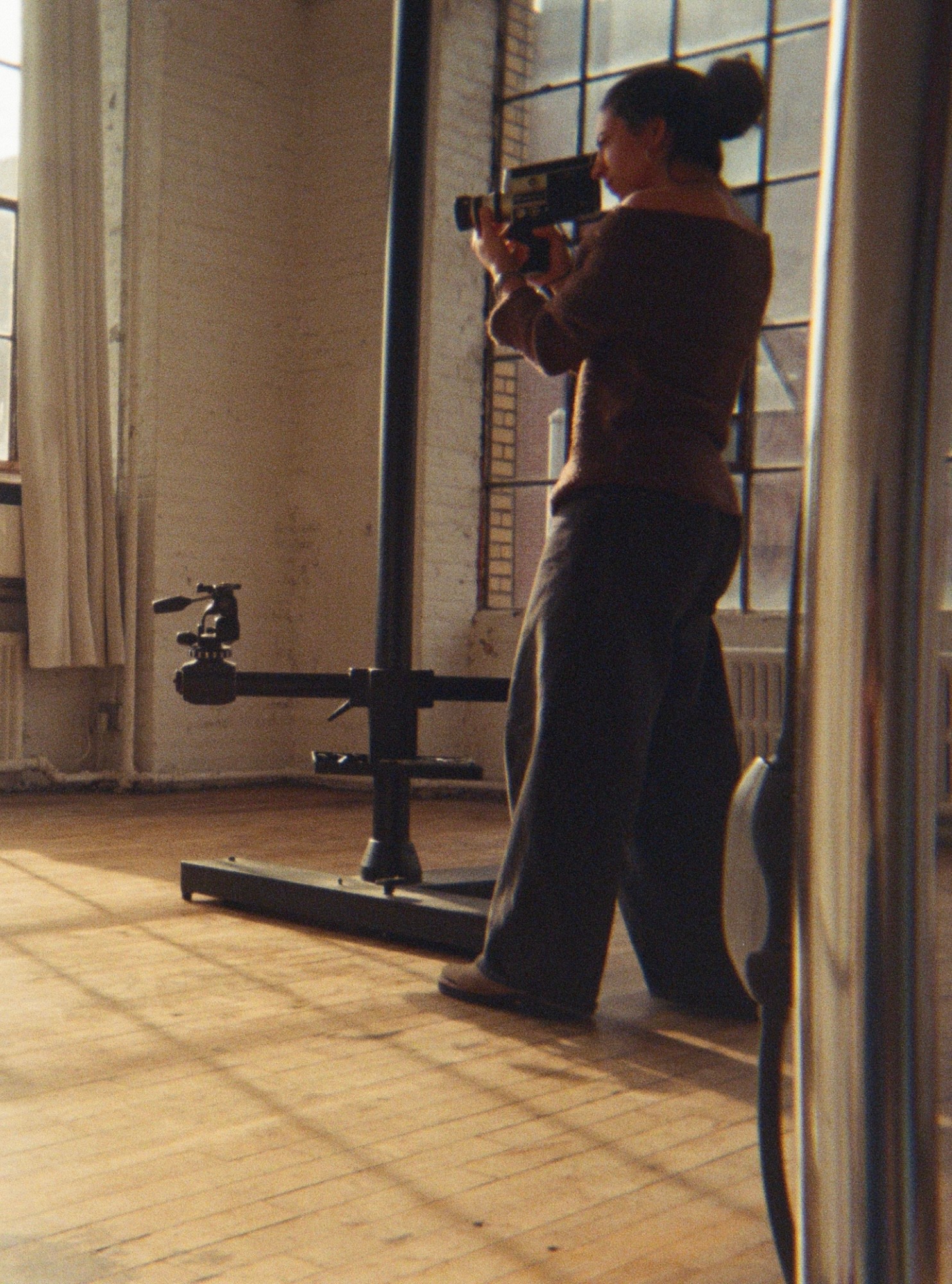 Person standing indoors, taking a photo with a camera, with sunlight casting shadows on the floor.