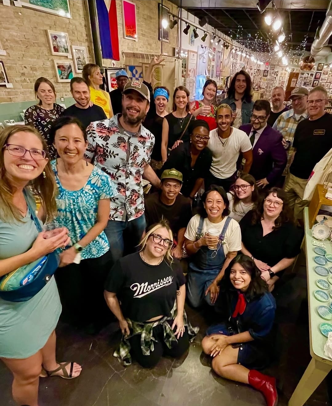 Group of people smiling and posing together in an art gallery or store with artwork and decorations on walls.