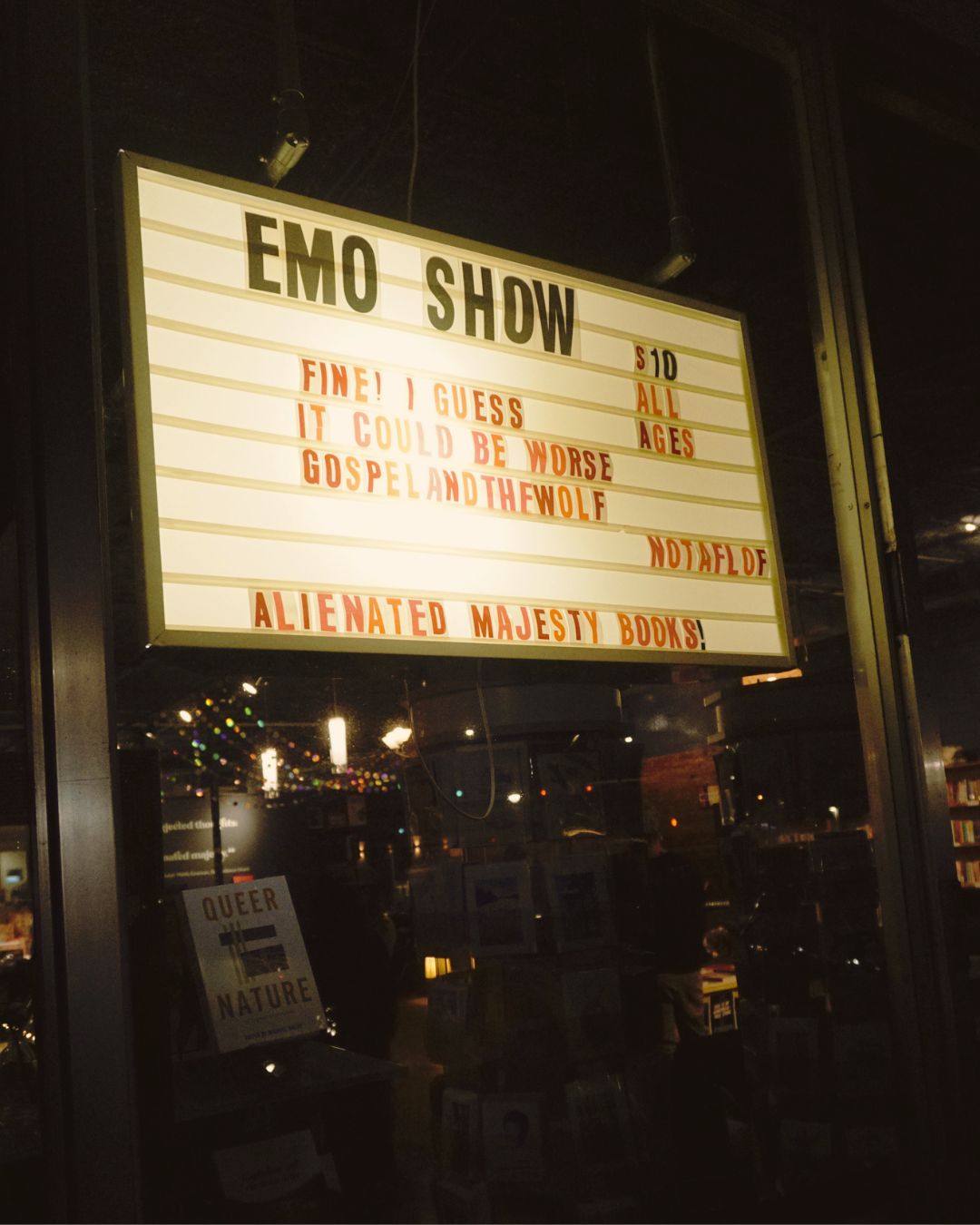 Illuminated sign reads 'EMO SHOW' with event details and ticket prices, inside a dark venue with reflections on glass.