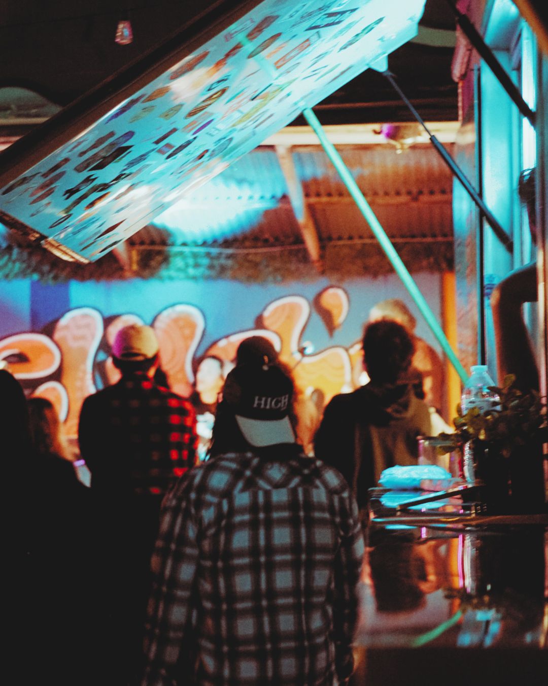 People watching a performer on stage with colorful lights and a large screen, in a lively indoor setting.