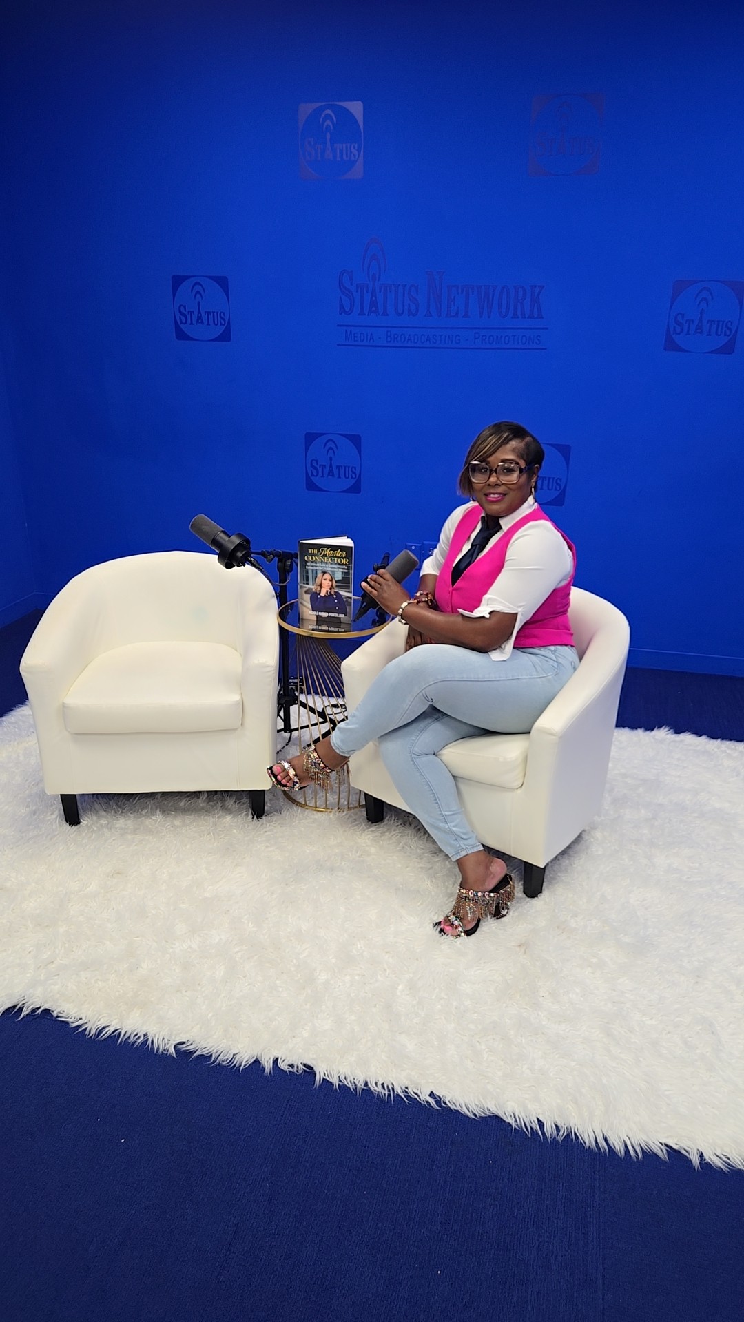 Woman sitting on a white armchair with a small table and a white armchair on a white rug, blue background.