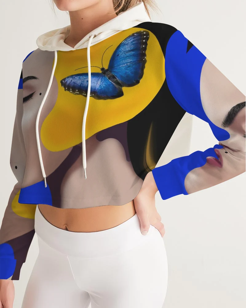 Person wearing a colorful hoodie with a blue butterfly design, standing with hand on hip, white pants, and a neutral background.