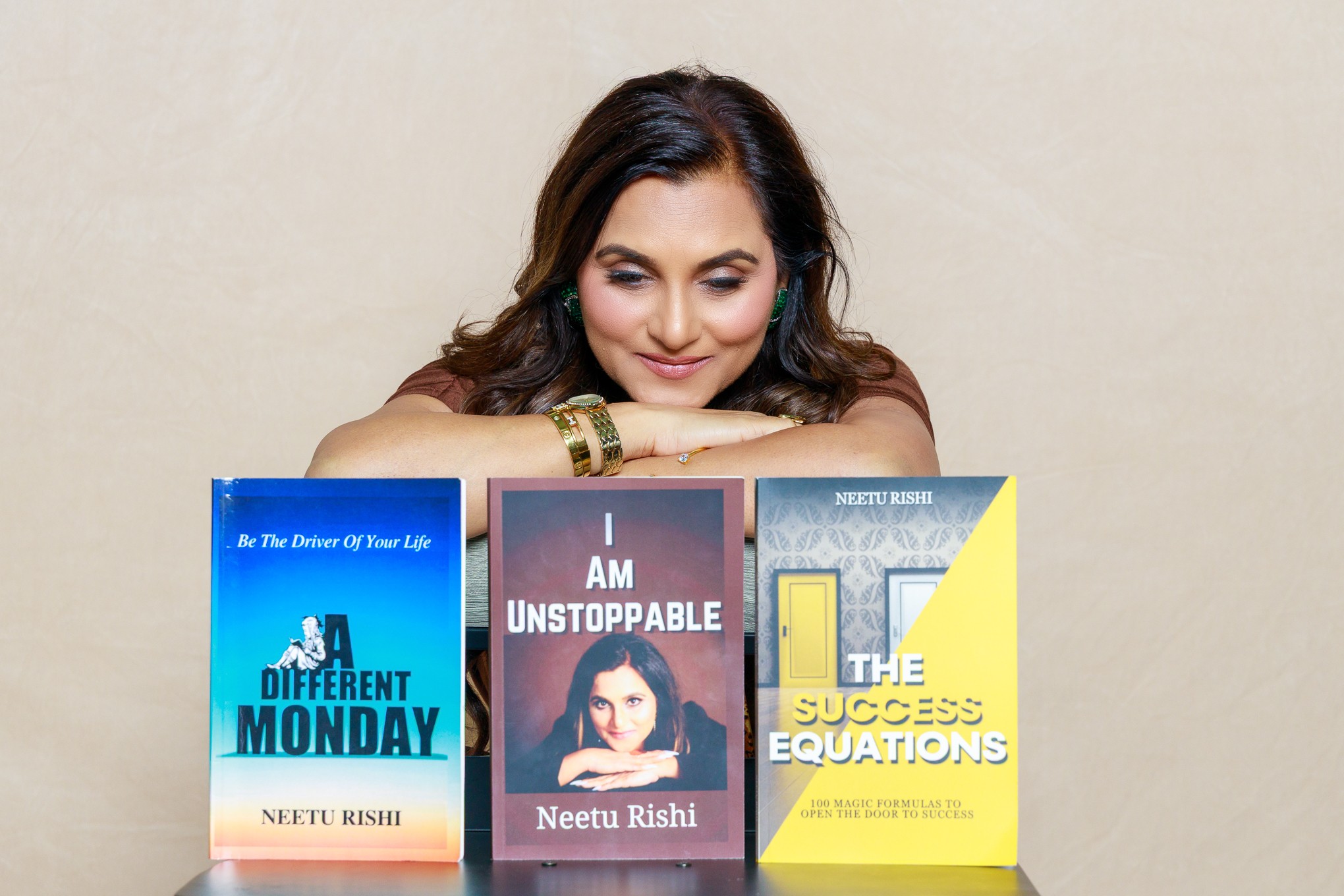 Woman with dark hair resting her chin on a table, smiling, with three books in front of her, against a plain background.