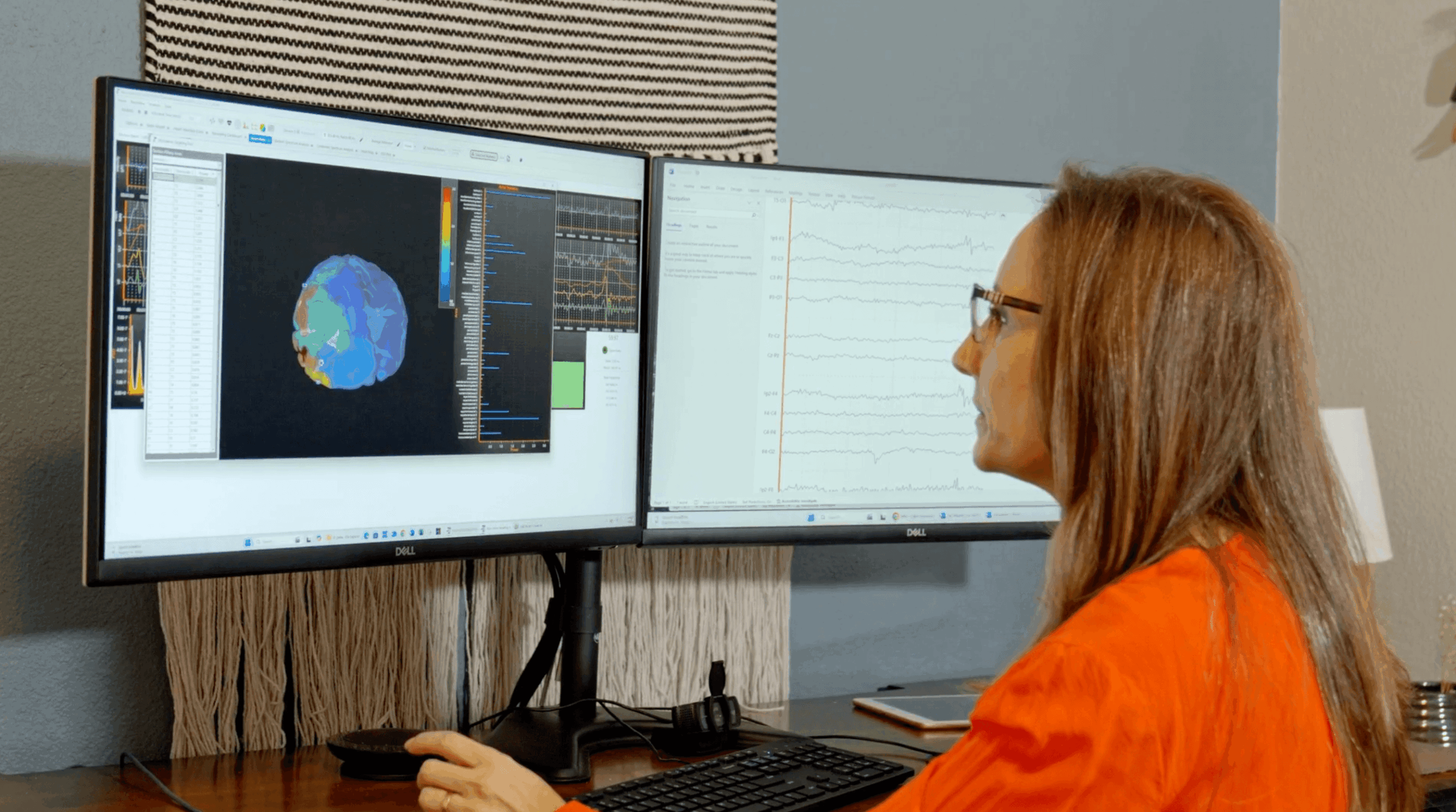 Woman with glasses and red hair working at dual computer monitors displaying scientific data and images.