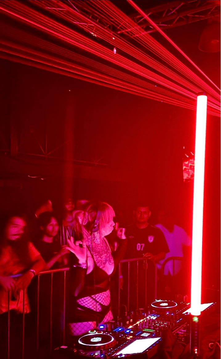People at a nightclub with red laser lights and a tall illuminated pole, some dancing and watching the scene.