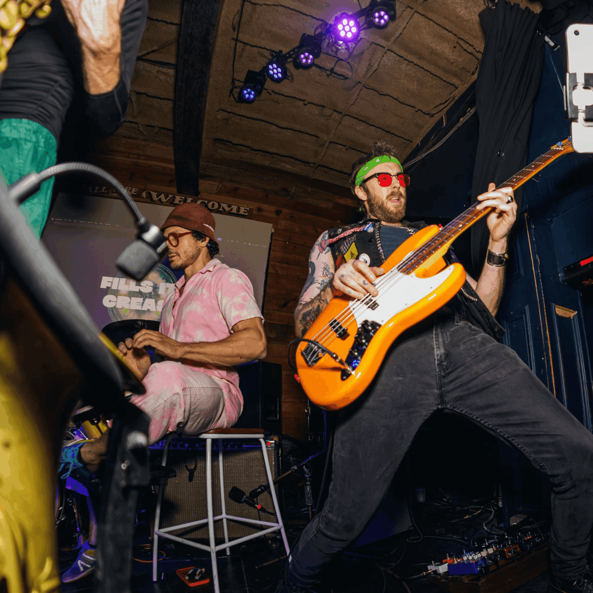 Two musicians perform on stage, one playing bass guitar and the other on keyboard, under stage lights.