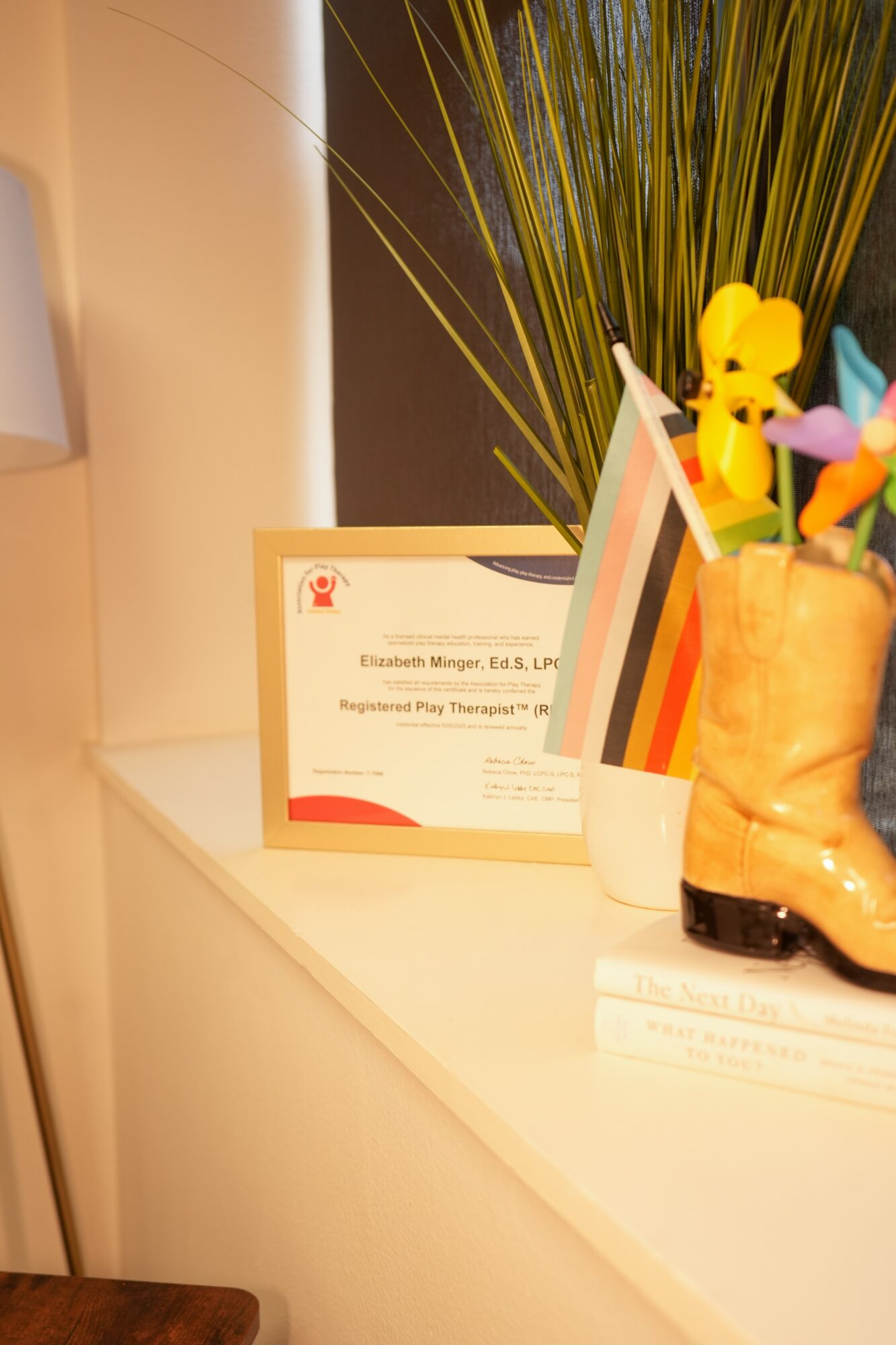 Certificate, colorful flowers, and a small rainbow flag on a white surface, with a plant in the background.