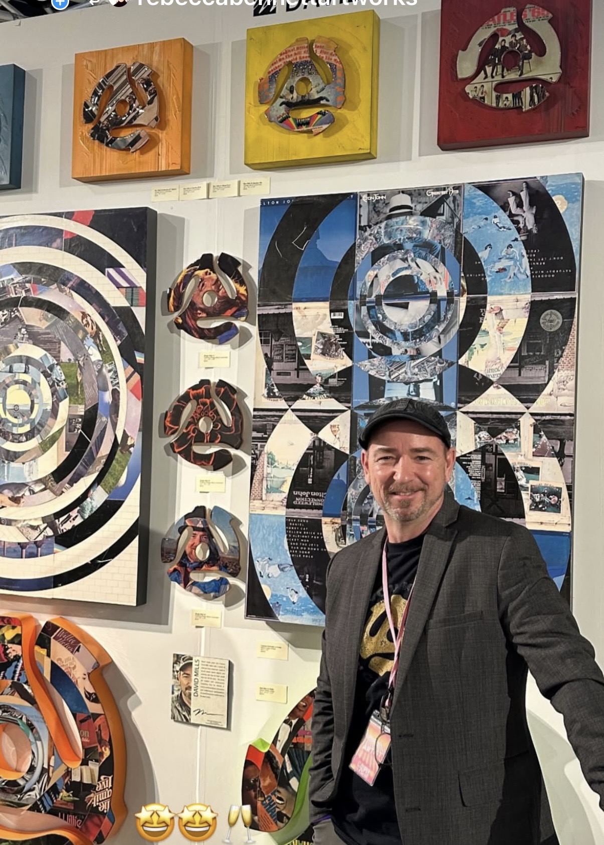 Man in black jacket and cap standing in front of colorful abstract artwork at an art gallery.