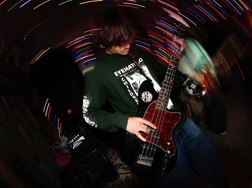 Person with dark hair playing a guitar in a dark setting with colorful light streaks.