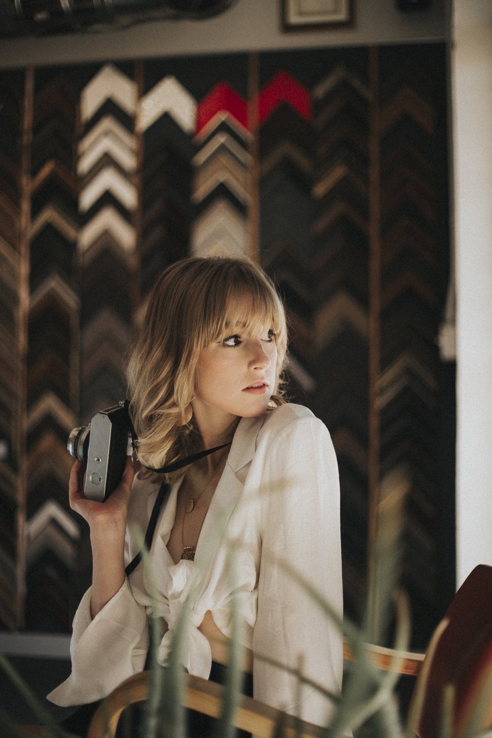 Young woman with shoulder-length hair holding a phone, looking to the side, in front of a patterned background.