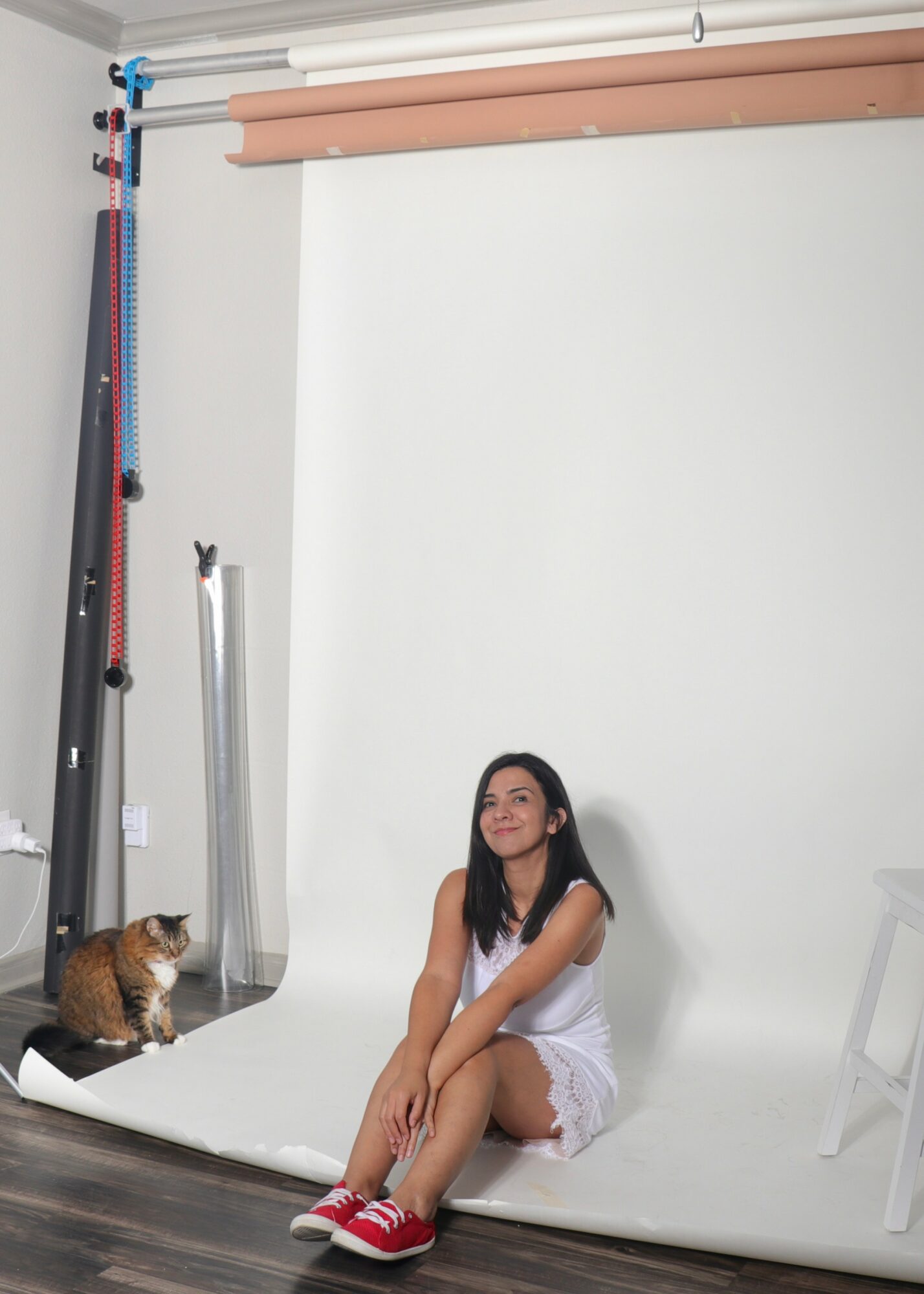 Young woman sitting on a white backdrop with a cat nearby, in a photography studio setting.