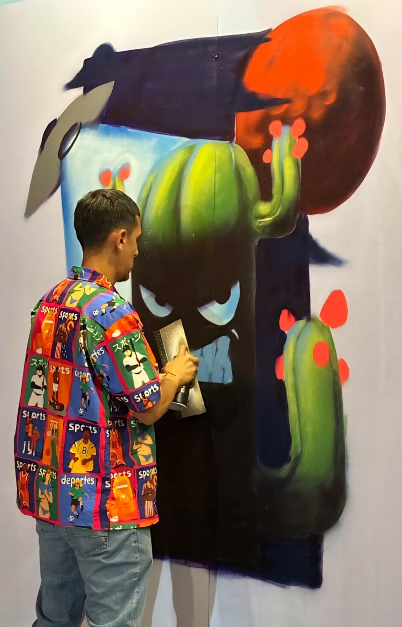 Person in colorful jacket painting a large, abstract mural with green, orange, and blue shapes on a black background.
