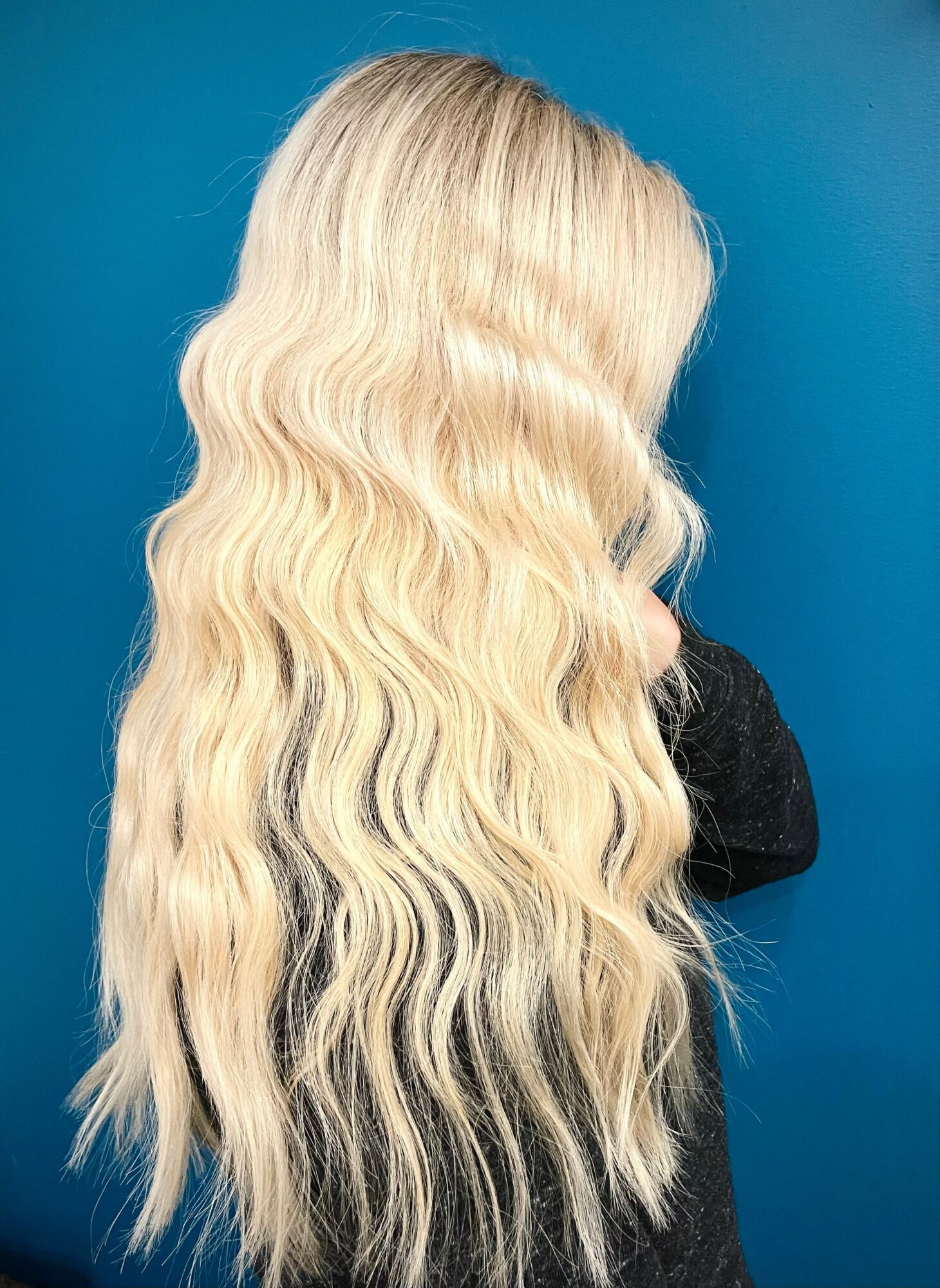 Back view of long, wavy blonde hair against a blue background.