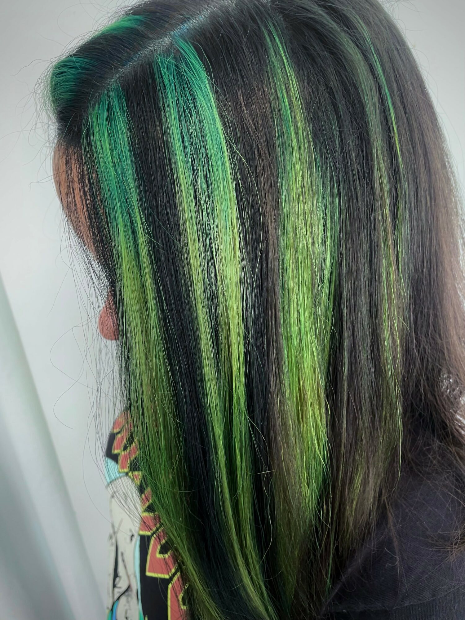 Side view of straight hair with green and black streaks, shiny and smooth, against a plain background.