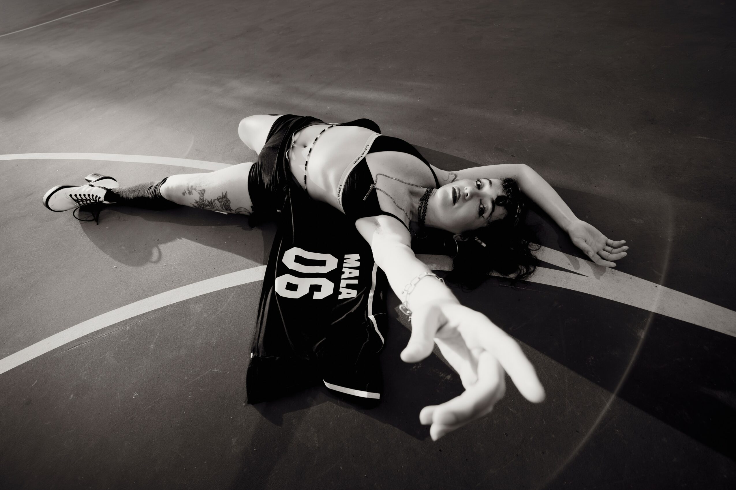A woman lies on a basketball court, reaching out with her hand, wearing sportswear and sneakers.
