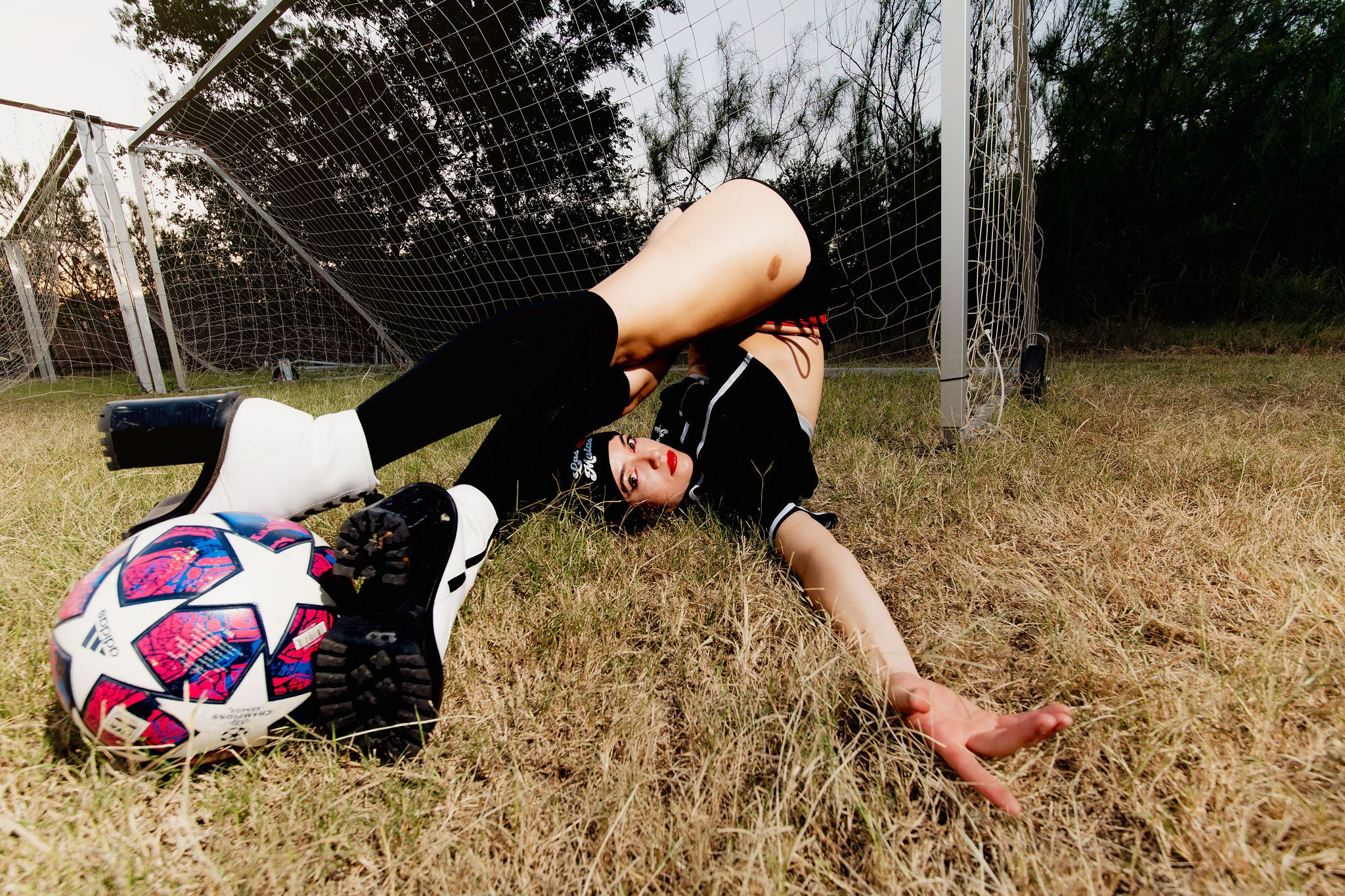 Person lying on grass with a soccer ball, fence, and trees in background, appearing upside down.