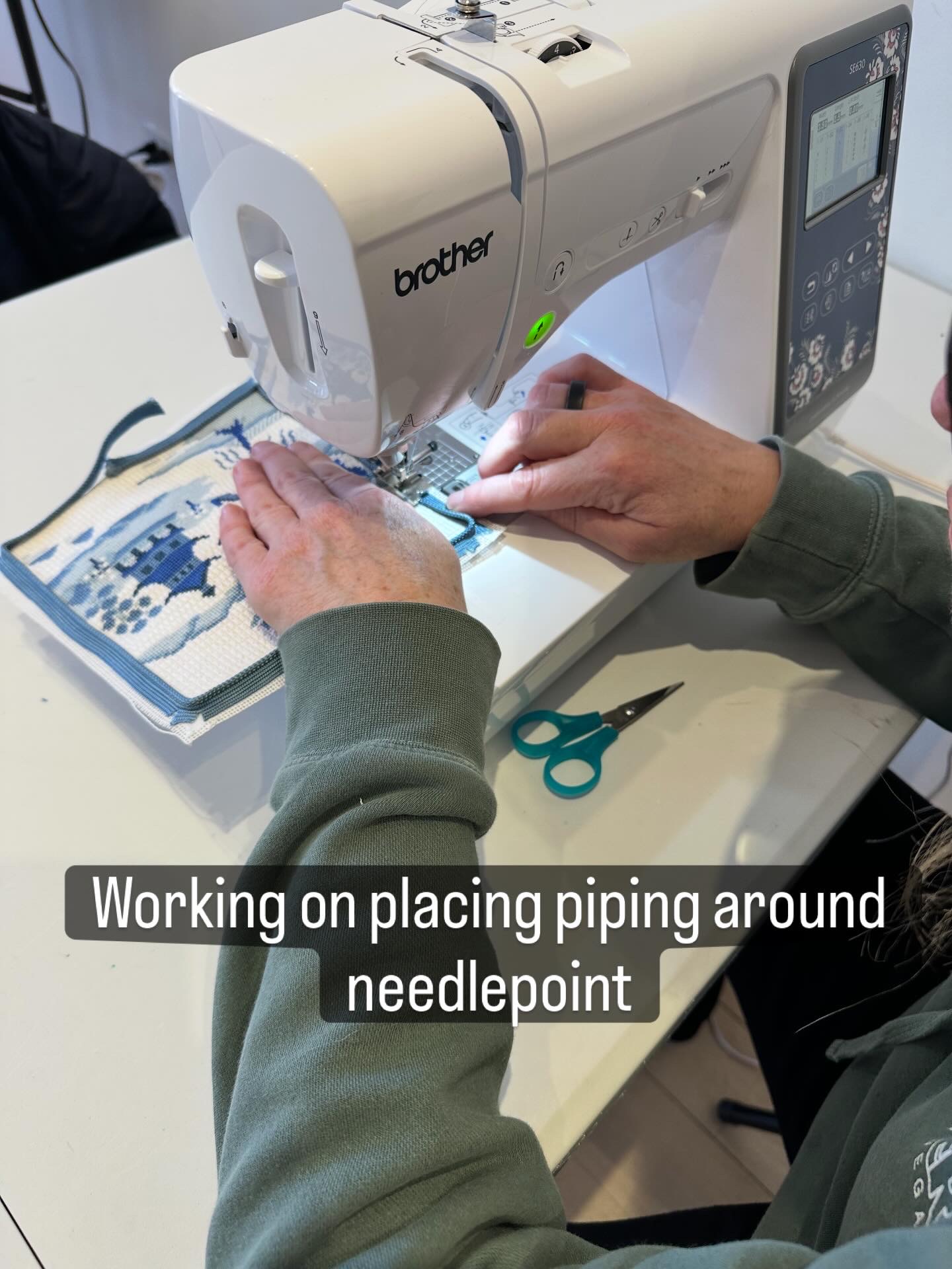 Person sewing fabric with a Brother sewing machine, working on piping around a needlepoint, with scissors nearby.