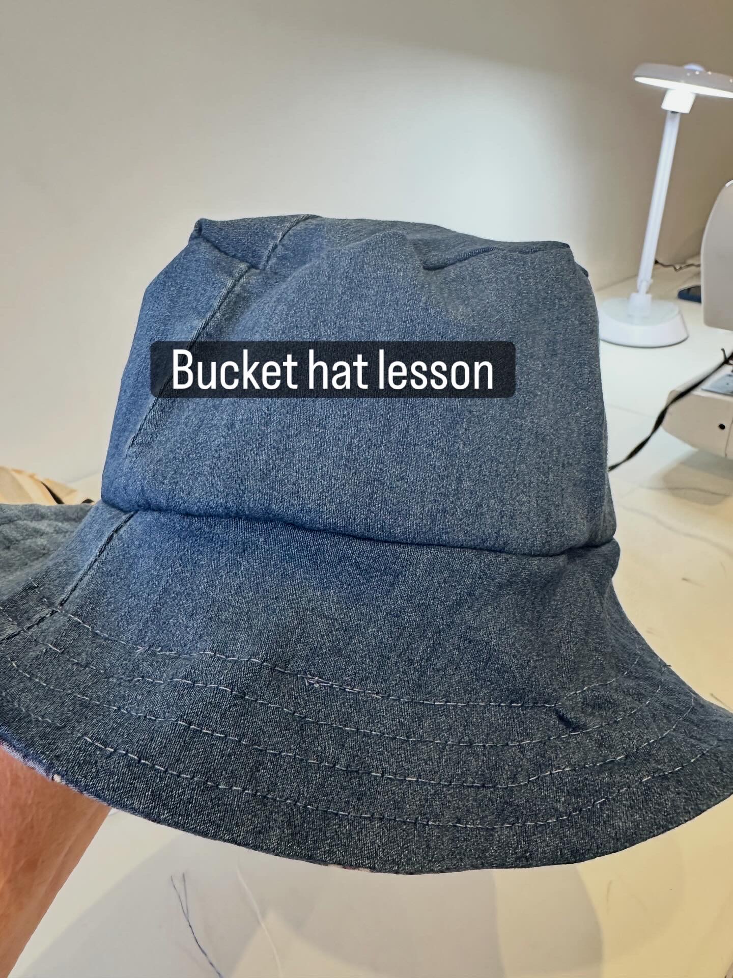 Bucket hat with text 'Bucket hat lesson' on it, placed on a table with a lamp in the background.