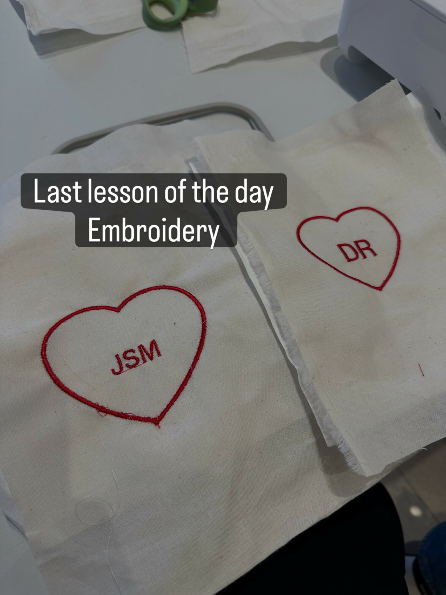 Two white cloths with red embroidered hearts and initials, on a table with sewing tools, captioned 'Last lesson of the day Embroidery'.
