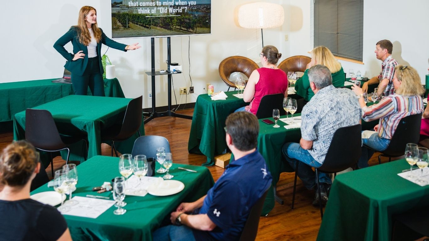 Woman presenting to seated group in a conference room with green tablecloths and glasses on tables.